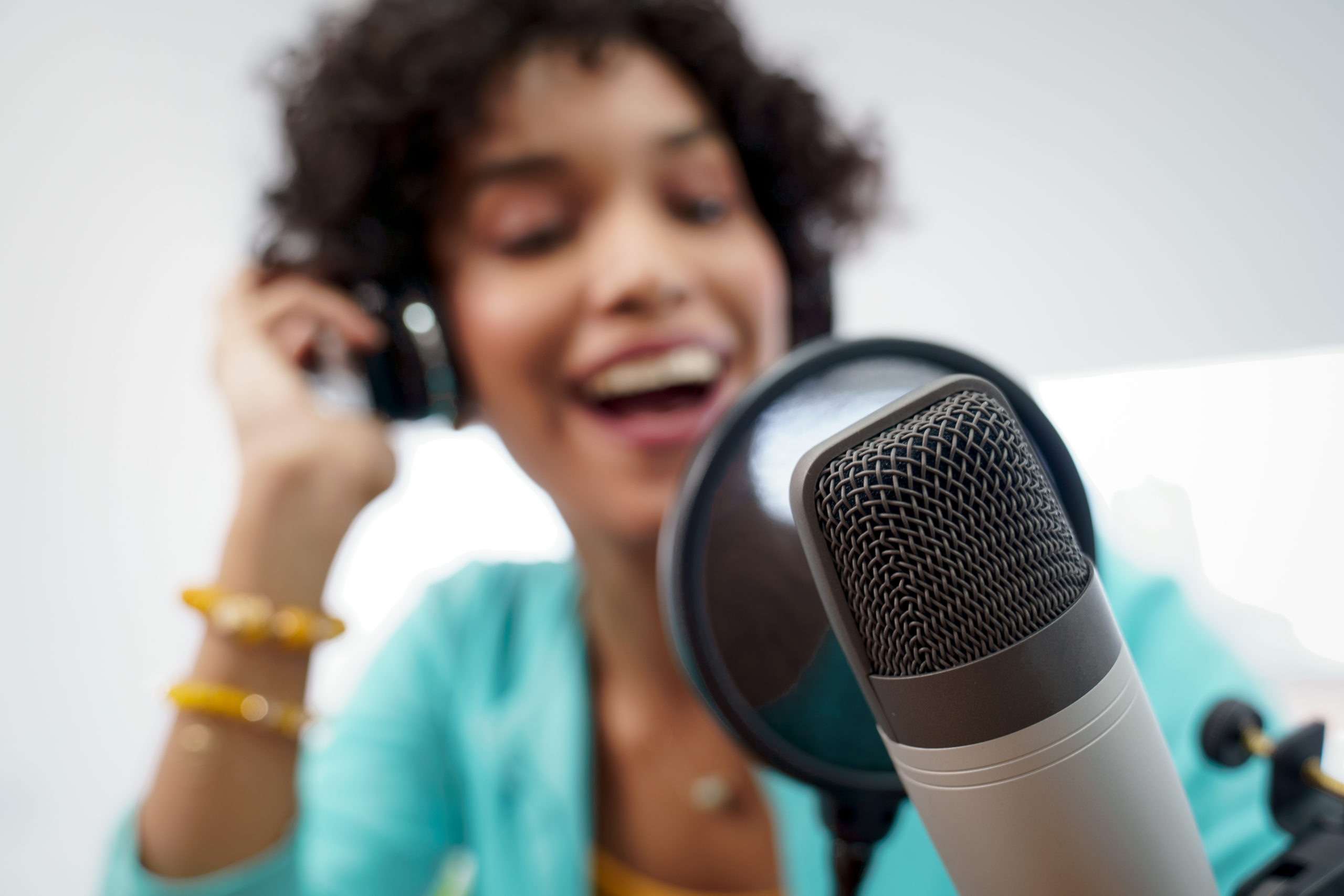 Good looking young black female making an online podcast recording for her online show. Attractive millennial African American business woman using headphones in front of microphone for radio program.
