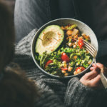 a woman eating a healthy salad from a bowl in her lap