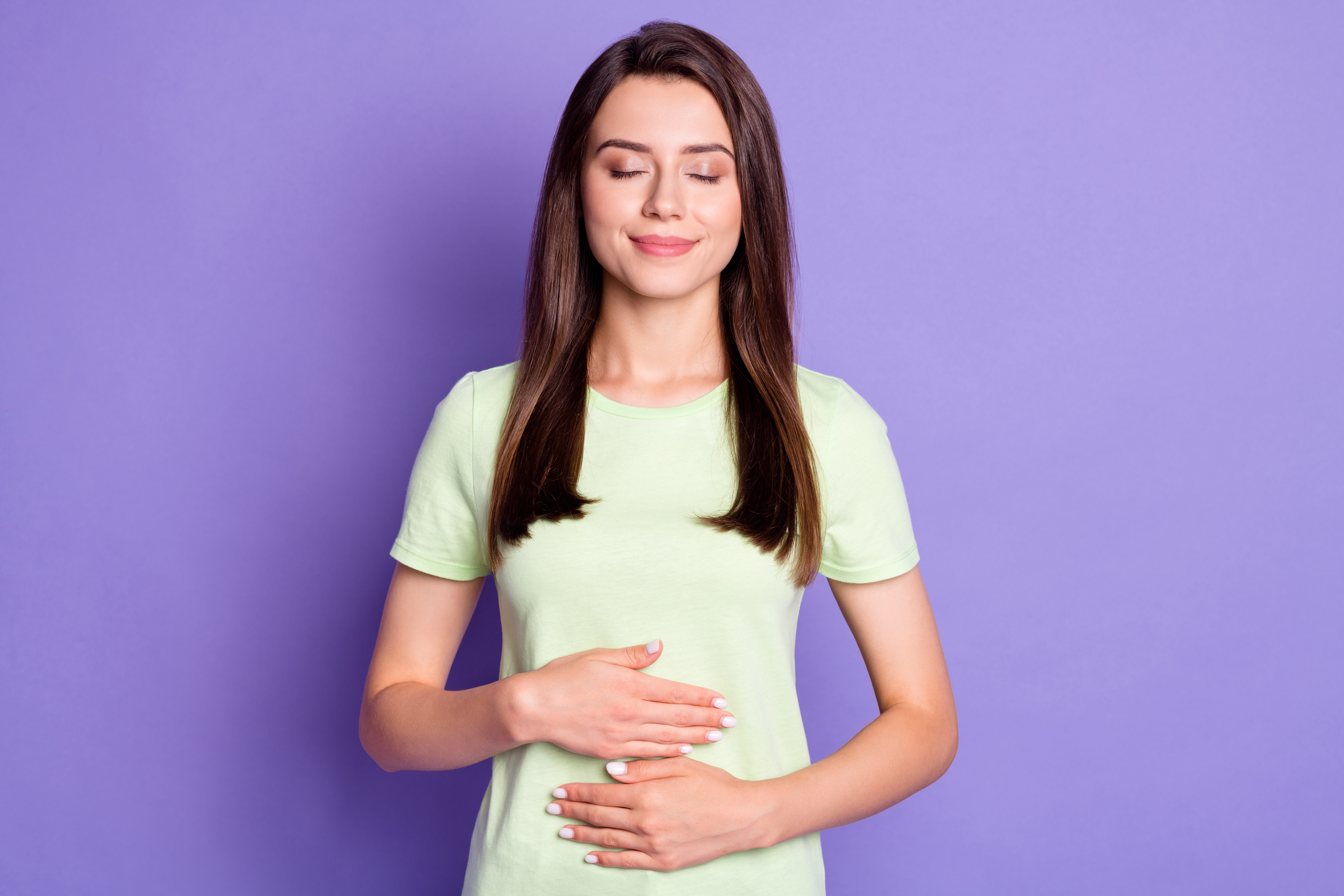 Photo portrait of dreamy girl keeping hands on tummy after delicious breakfast smiling isolated on vibrant purple color background.
