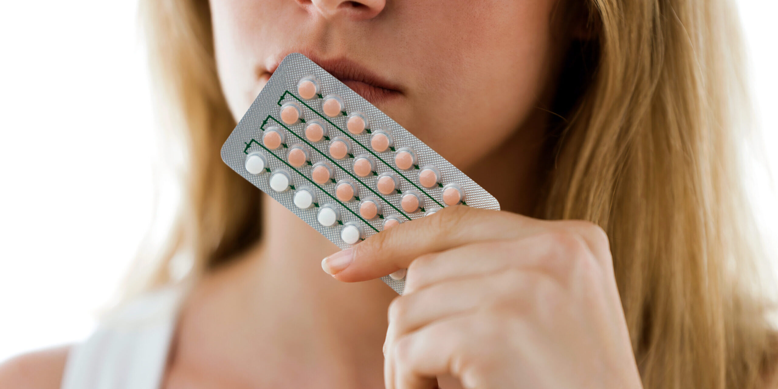 Shot of unhappy young woman holding contraceptive pills over white background.